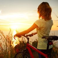 Young woman standing with bicycle watching sunset over the ocean